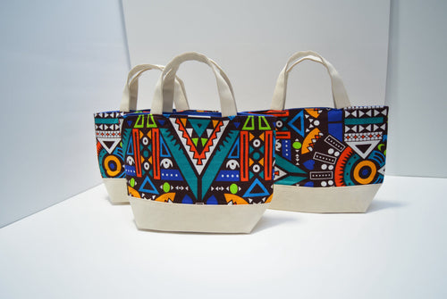 Three canvas tote bags with colorful geometric and tribal patterns, featuring cream-colored handles and bases, displayed on a white surface against a white background.