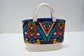 A canvas tote bag with a colorful geometric tribal pattern on the front and a solid cream-colored bottom panel and handles, set against a plain white studio background.