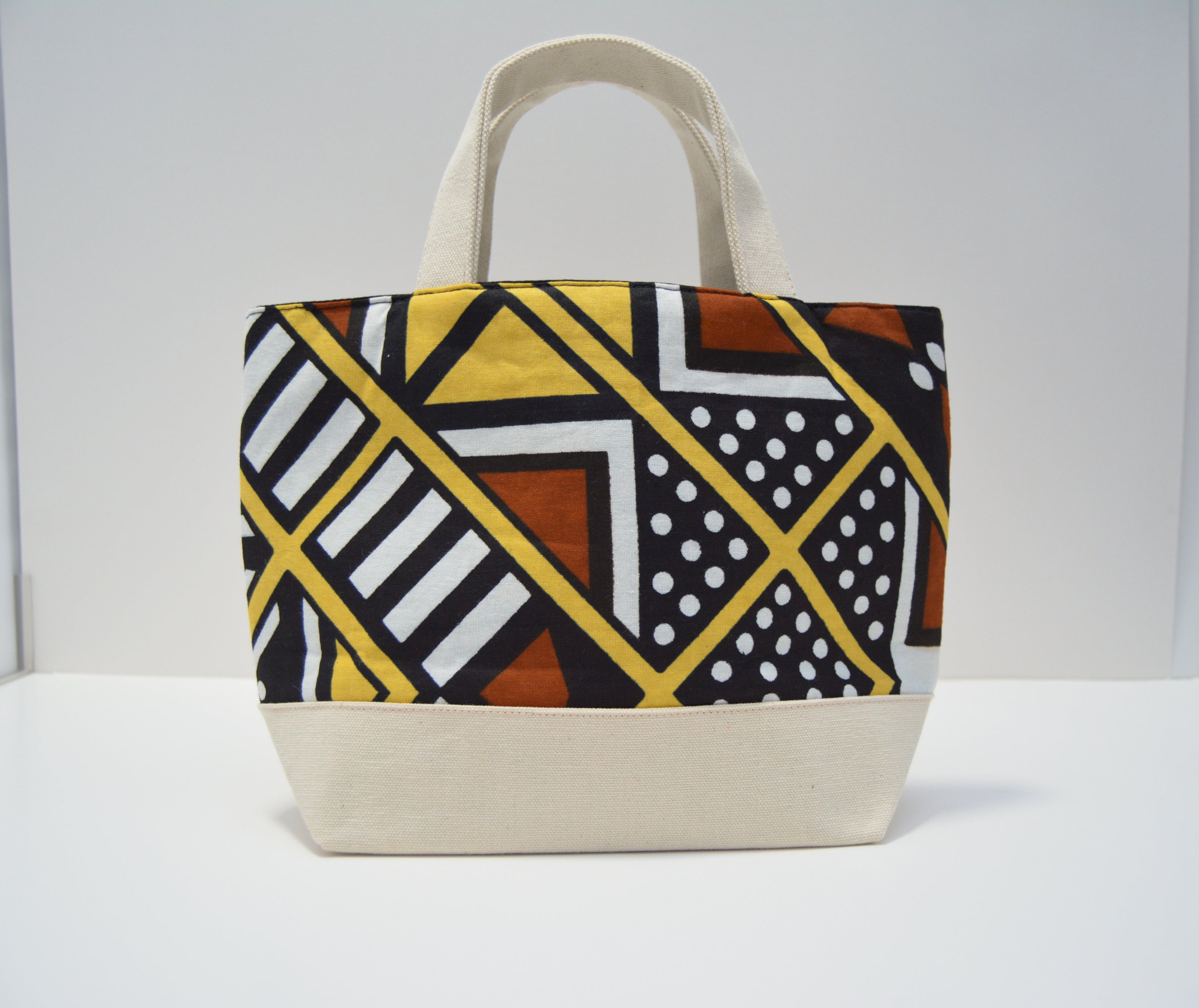 A canvas tote bag with a geometric African wax print pattern on the upper half and solid cream-colored canvas on the bottom base and handles, set against a plain white background.