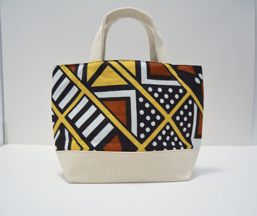 A canvas tote bag with a geometric African wax print pattern on the upper half and solid cream-colored canvas on the bottom base and handles, set against a plain white background.