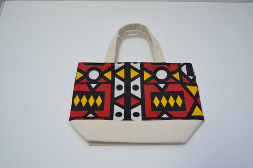 A canvas tote bag with a colorful geometric patterned front panel and solid beige handles and bottom base, photographed on a plain white background.
