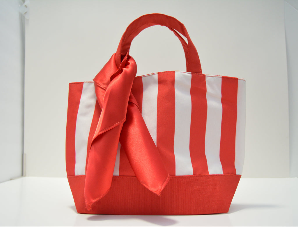 A red and white vertically striped fabric tote bag with a large red satin bow tied around the front, set against a plain white background.