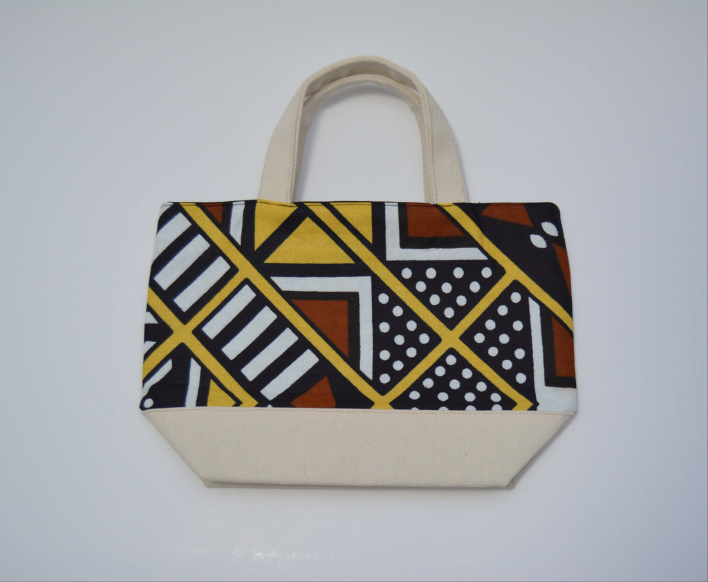 A canvas tote bag with a geometric African wax print pattern on the front panel and solid cream-colored canvas handles and base, shown against a plain light gray background.