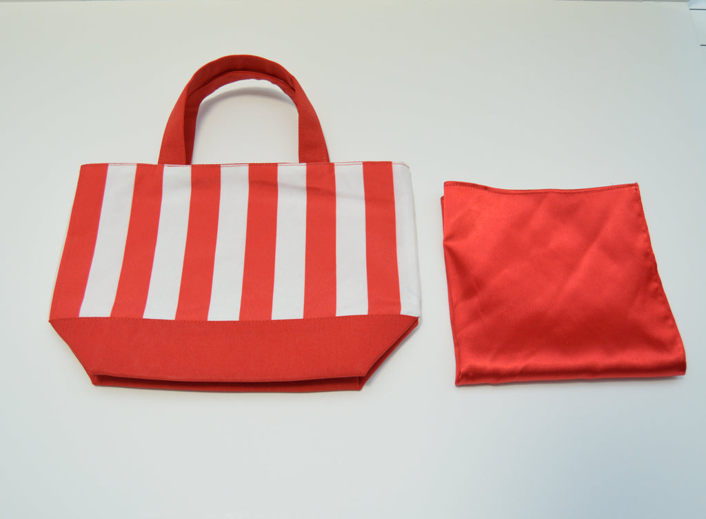 A red and white striped fabric tote bag with red handles, shown next to a folded red satin-like scarf on a white surface.