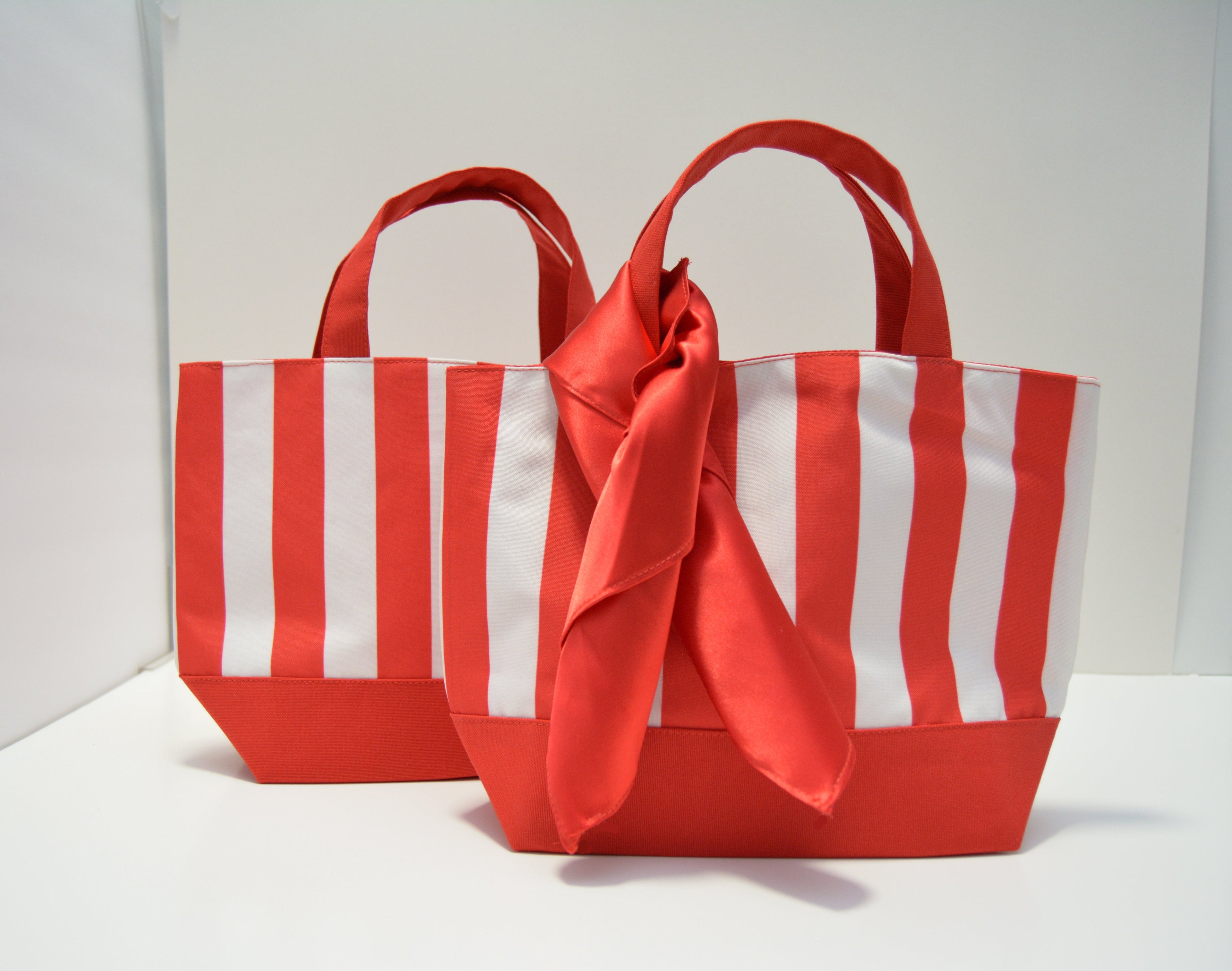 Two red and white striped fabric tote bags with satin ribbon handles, displayed on a white surface against a white background.